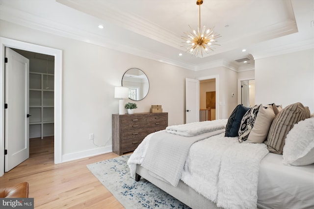 bedroom with an inviting chandelier, a raised ceiling, light wood-type flooring, a closet, and a walk in closet