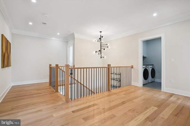 hallway featuring washer and dryer, light wood-type flooring, ornamental molding, and a notable chandelier