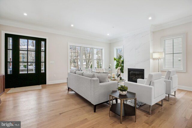 living room with a tile fireplace, ornamental molding, and light hardwood / wood-style flooring