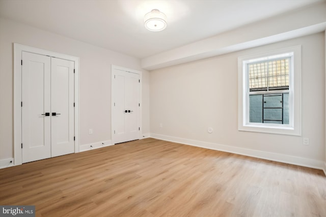 unfurnished bedroom featuring multiple closets and light hardwood / wood-style floors