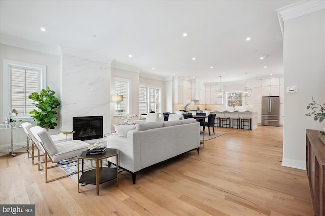 living room featuring a high end fireplace, ornamental molding, and light hardwood / wood-style flooring