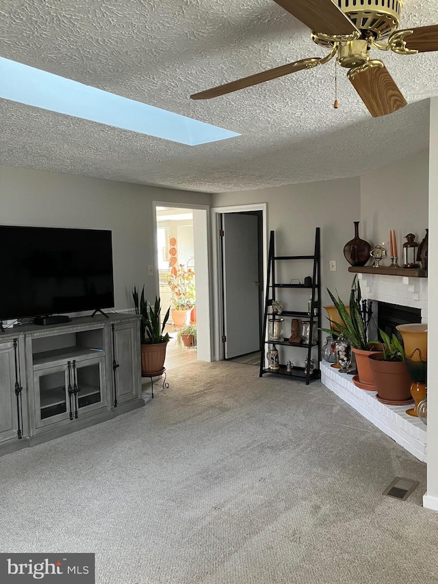 living room with carpet, ceiling fan, a brick fireplace, and a skylight