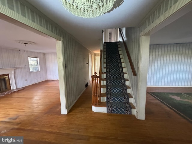 stairs featuring hardwood / wood-style flooring, wooden walls, and an inviting chandelier