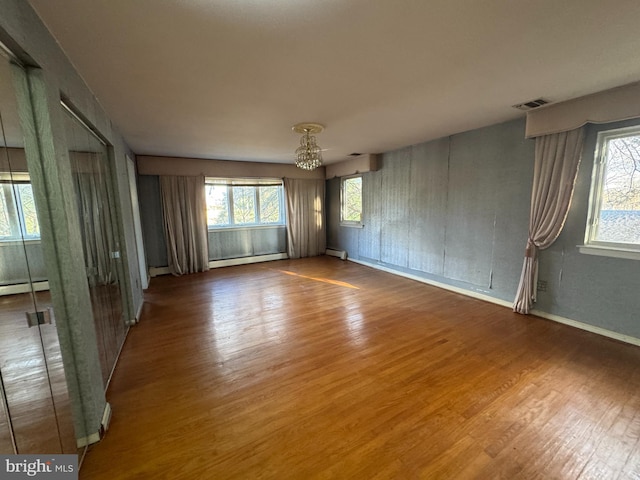 unfurnished room with baseboard heating, a wealth of natural light, a chandelier, and hardwood / wood-style flooring