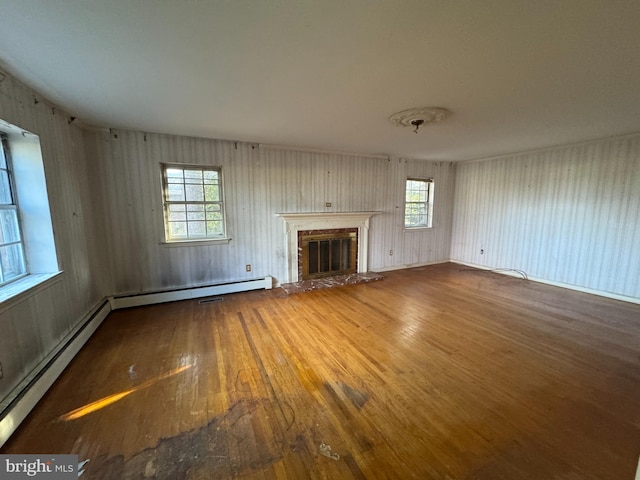 unfurnished living room featuring hardwood / wood-style flooring, baseboard heating, and a healthy amount of sunlight