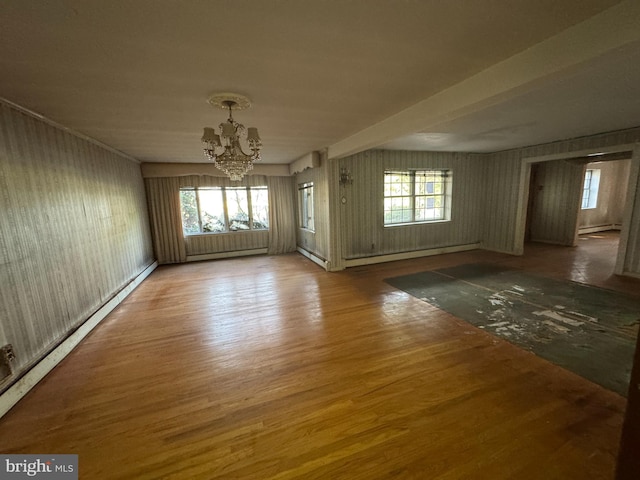 empty room featuring wood-type flooring, an inviting chandelier, and baseboard heating