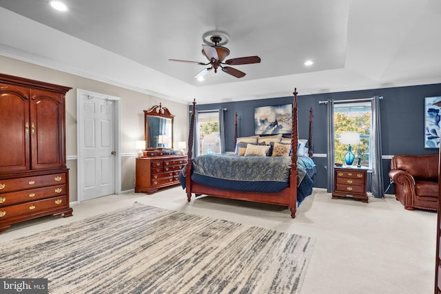 bedroom featuring light carpet, multiple windows, a tray ceiling, and ceiling fan