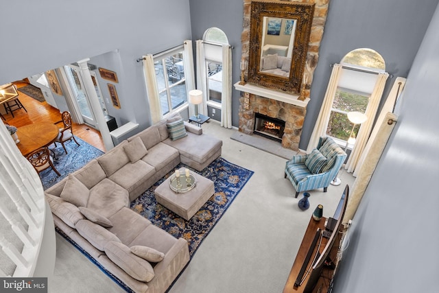 living room featuring carpet, a towering ceiling, decorative columns, and a stone fireplace