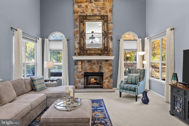 carpeted living room with a high ceiling, a stone fireplace, and a healthy amount of sunlight