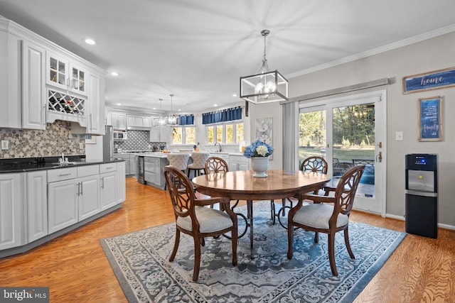 dining space with ornamental molding, light hardwood / wood-style floors, a notable chandelier, and sink