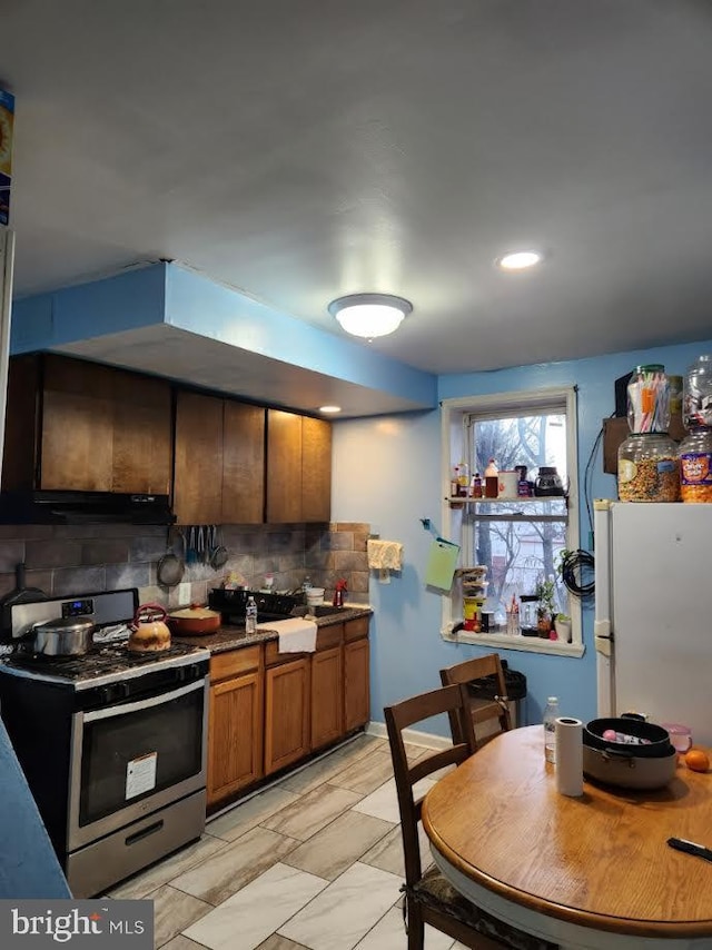 kitchen with decorative backsplash, white refrigerator, and stainless steel range oven