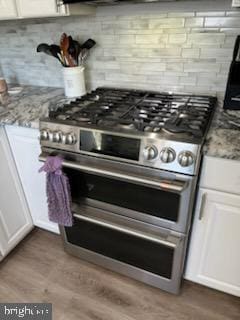 kitchen featuring light stone countertops, light wood-type flooring, white cabinetry, and range with two ovens