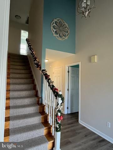 staircase featuring a high ceiling, hardwood / wood-style flooring, and an inviting chandelier