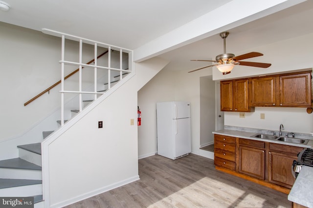 kitchen with stainless steel gas range oven, sink, ceiling fan, light hardwood / wood-style floors, and white fridge