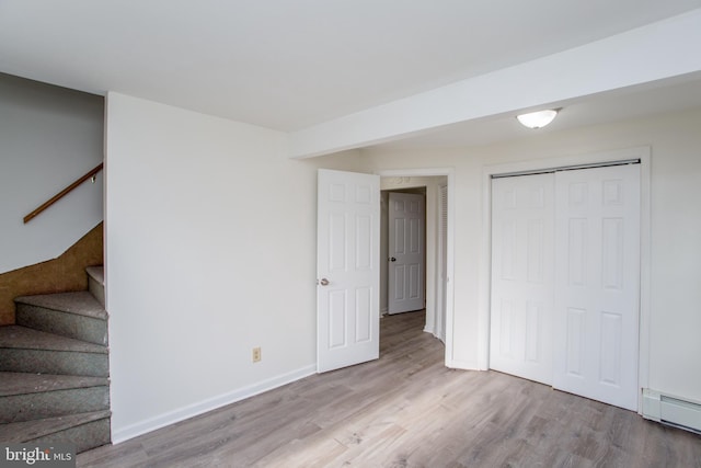 basement featuring light hardwood / wood-style flooring and a baseboard heating unit