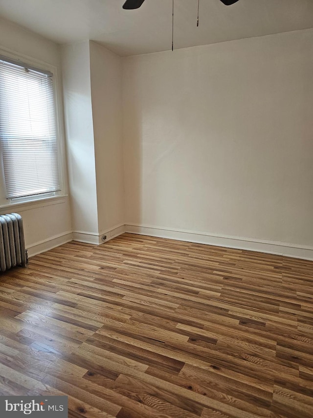 empty room with dark hardwood / wood-style floors, ceiling fan, and radiator