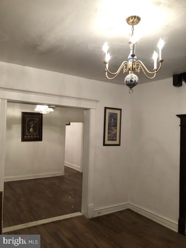 spare room featuring dark wood-type flooring and a notable chandelier