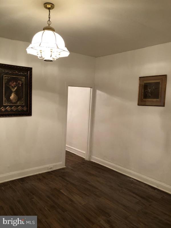 unfurnished room with an inviting chandelier and dark wood-type flooring