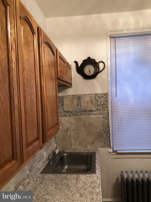 kitchen featuring light stone counters, radiator heating unit, and sink