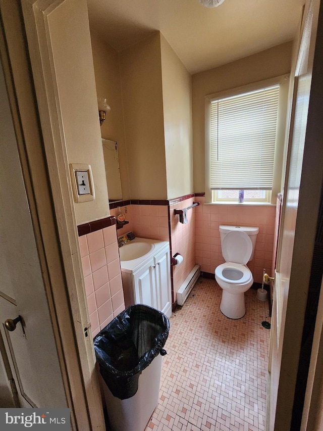 bathroom with a baseboard heating unit, tile patterned floors, sink, toilet, and tile walls