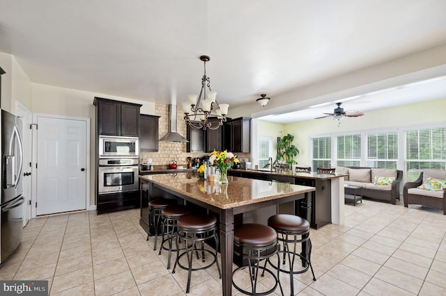 kitchen featuring wall chimney exhaust hood, backsplash, pendant lighting, a breakfast bar, and appliances with stainless steel finishes