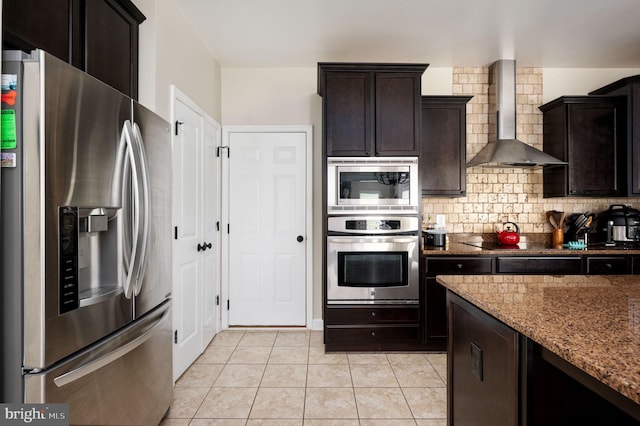 kitchen with backsplash, wall chimney range hood, light stone countertops, dark brown cabinets, and stainless steel appliances