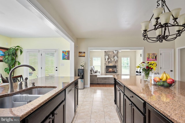 kitchen featuring dishwasher, an inviting chandelier, a stone fireplace, sink, and light stone counters