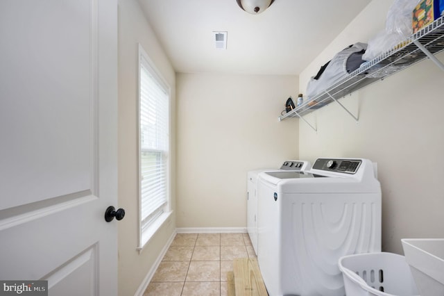 clothes washing area with washing machine and dryer, a wealth of natural light, and light tile patterned floors