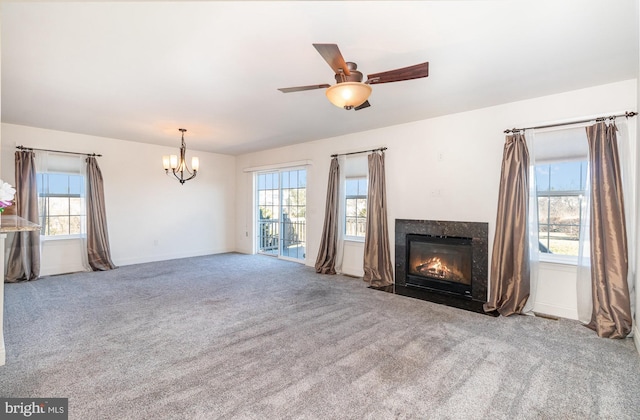 unfurnished living room featuring a premium fireplace, ceiling fan with notable chandelier, carpet flooring, and a wealth of natural light