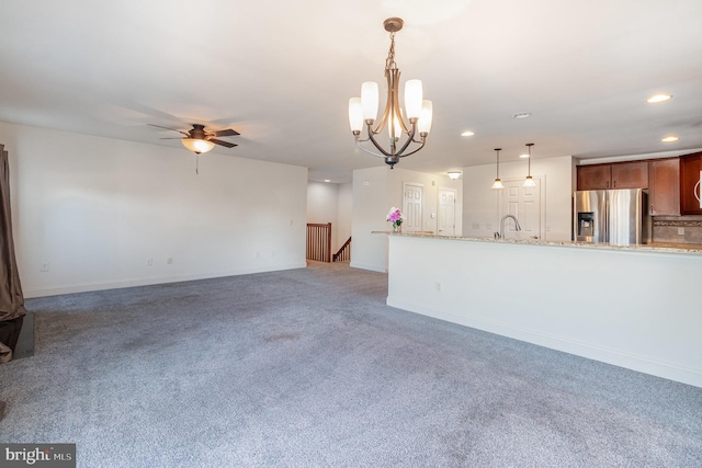 unfurnished living room with sink, ceiling fan with notable chandelier, and carpet flooring