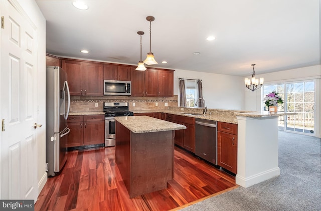 kitchen featuring sink, hanging light fixtures, stainless steel appliances, light stone counters, and a kitchen island