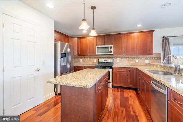 kitchen featuring sink, appliances with stainless steel finishes, hanging light fixtures, a center island, and light stone counters