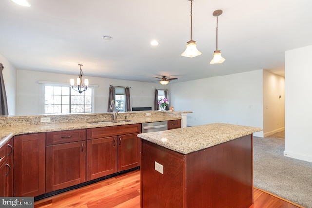 kitchen with pendant lighting, sink, dishwasher, a center island, and light stone counters