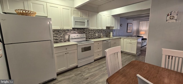 kitchen with white appliances, white cabinets, light hardwood / wood-style flooring, beamed ceiling, and light stone counters