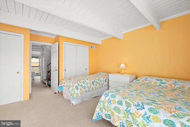 bedroom featuring beam ceiling, light carpet, and a closet