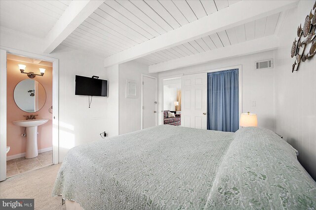 bedroom featuring beamed ceiling, light tile patterned floors, connected bathroom, and sink