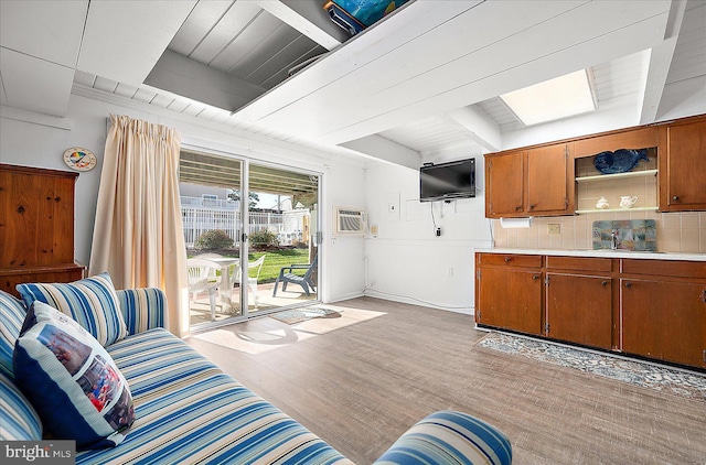 living room with beamed ceiling, a skylight, light hardwood / wood-style flooring, and wooden ceiling