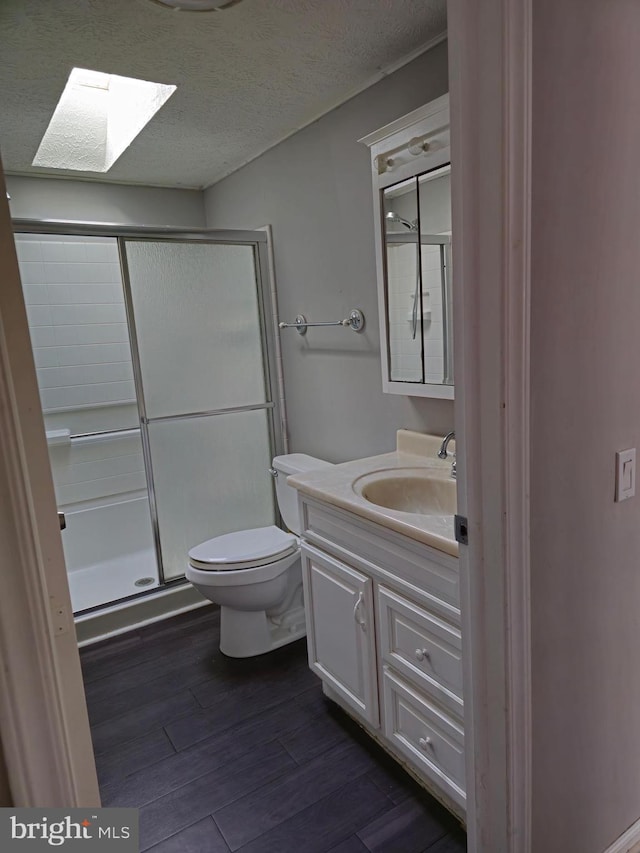 bathroom with a skylight, vanity, a textured ceiling, hardwood / wood-style floors, and a shower with shower door