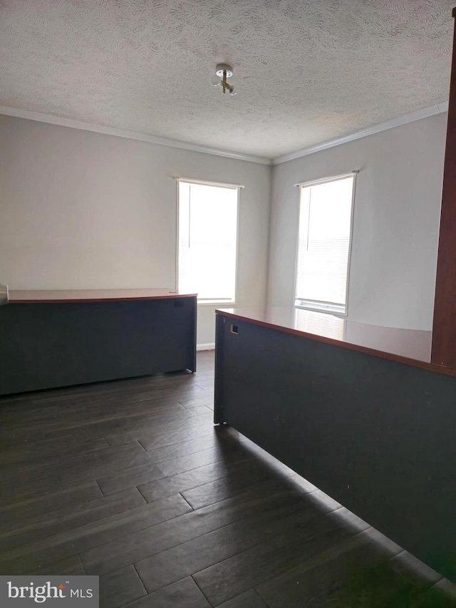 empty room with a textured ceiling, a healthy amount of sunlight, and dark wood-type flooring