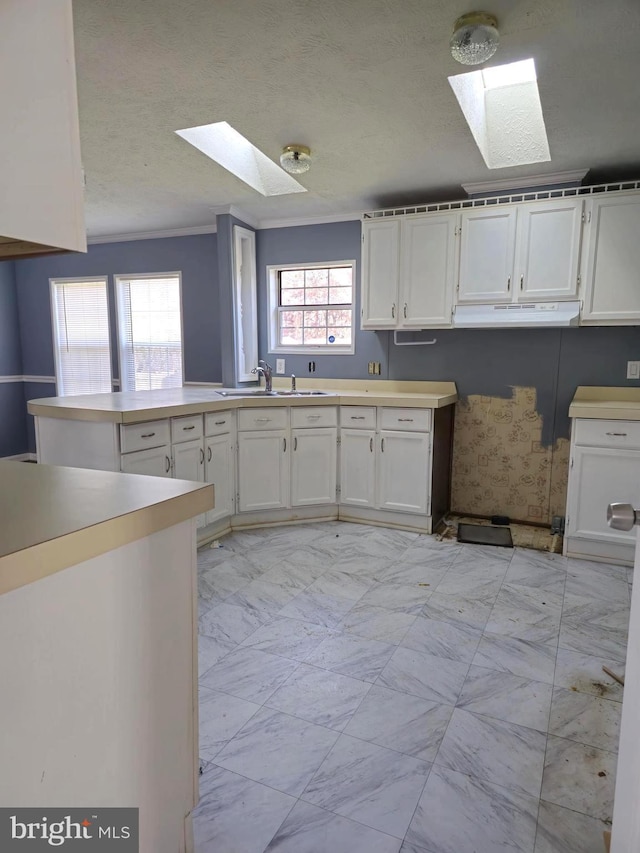 kitchen with a skylight, a textured ceiling, crown molding, sink, and white cabinets