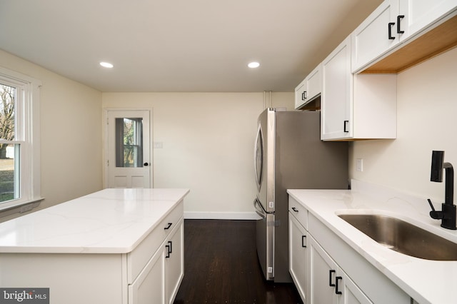 kitchen with dark wood-type flooring, sink, stainless steel fridge, light stone counters, and white cabinetry