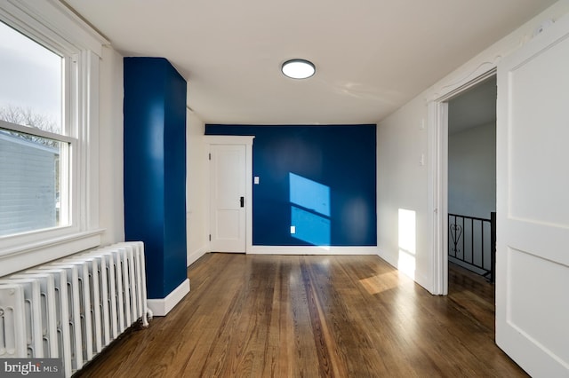 empty room with radiator, dark wood-type flooring, and a healthy amount of sunlight