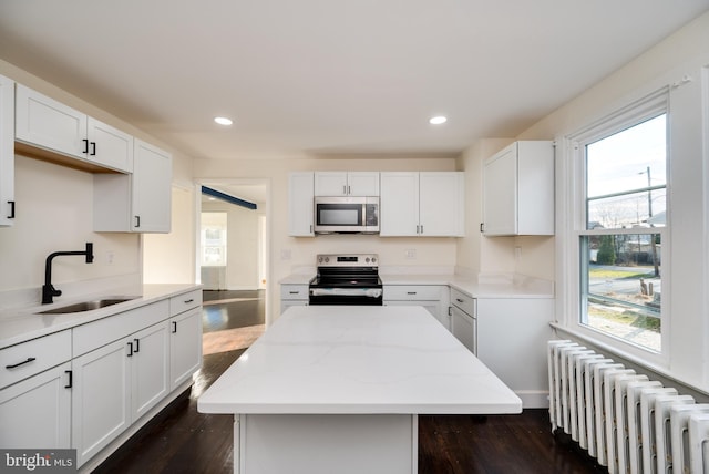 kitchen with stainless steel appliances, sink, radiator heating unit, dark hardwood / wood-style floors, and a kitchen island