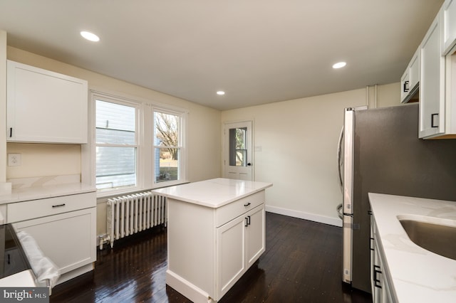 kitchen with light stone countertops, dark hardwood / wood-style floors, white cabinetry, and radiator