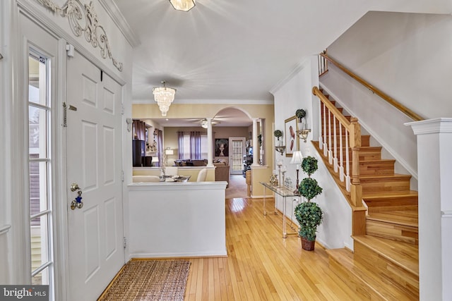 entryway with ornate columns, crown molding, light hardwood / wood-style flooring, and ceiling fan with notable chandelier