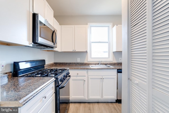 kitchen featuring sink, light wood-type flooring, appliances with stainless steel finishes, dark stone counters, and white cabinets