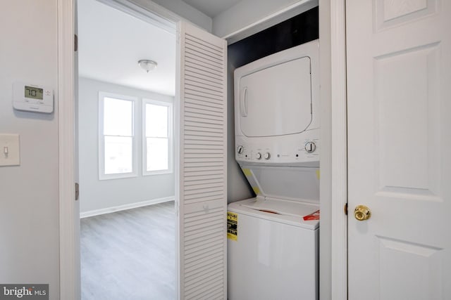 washroom with hardwood / wood-style flooring and stacked washer / drying machine