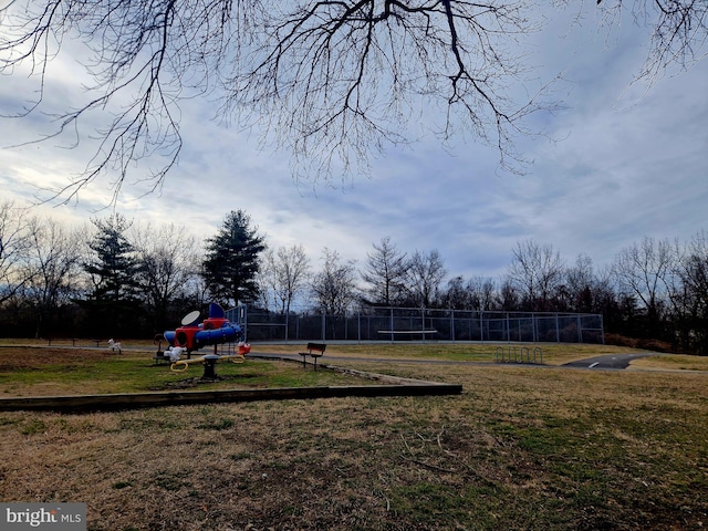 view of playground featuring a tennis court, a lawn, and fence