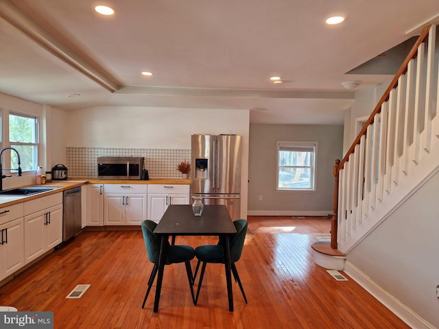 kitchen with white cabinetry, sink, stainless steel appliances, tasteful backsplash, and light hardwood / wood-style floors