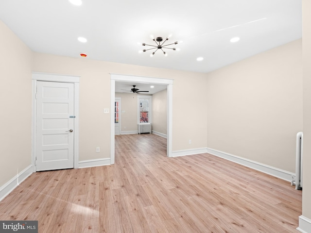 empty room with radiator, light hardwood / wood-style flooring, and ceiling fan with notable chandelier